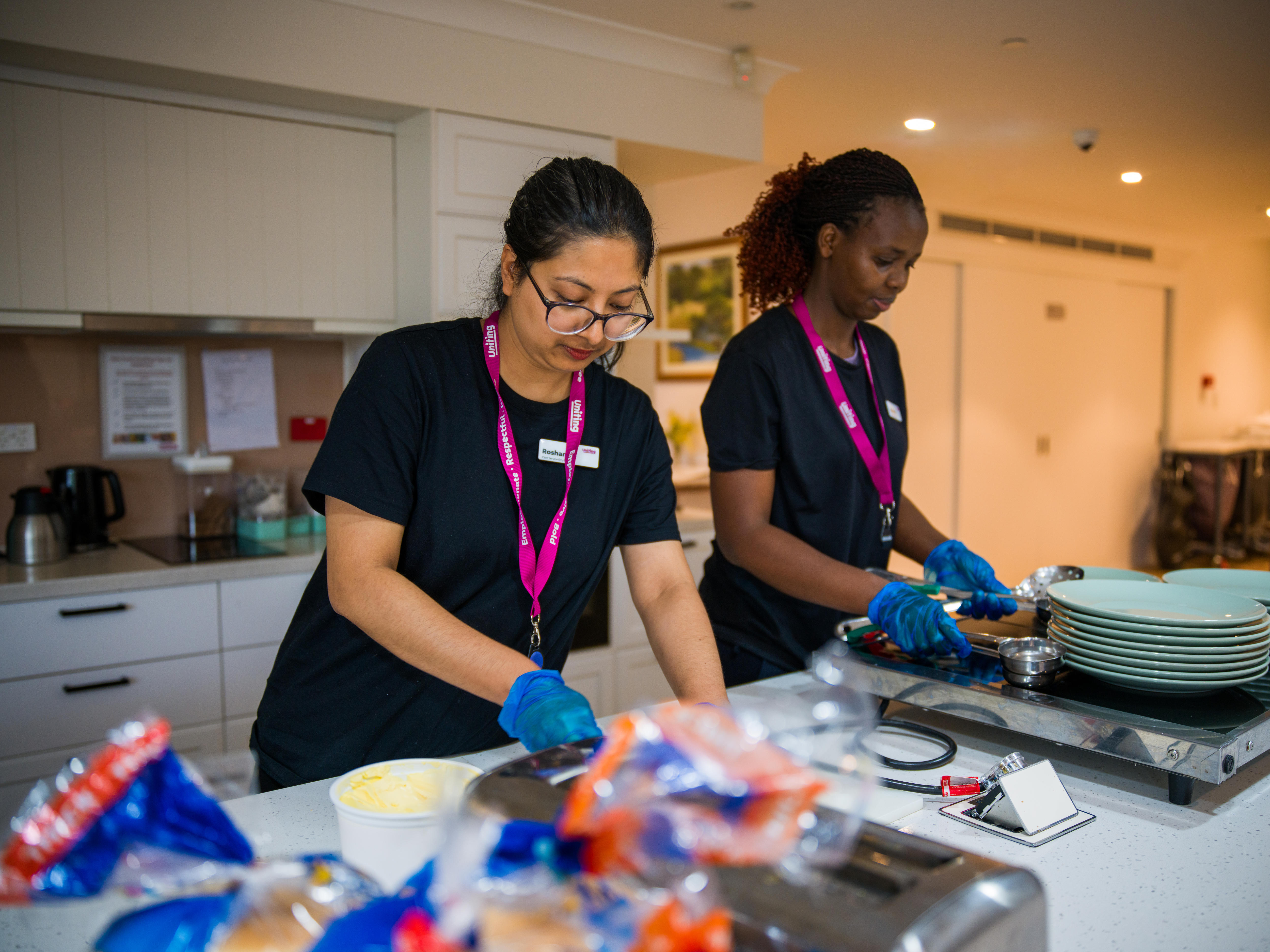 Two immigrant aged care workers preparing food for aged care residents.
