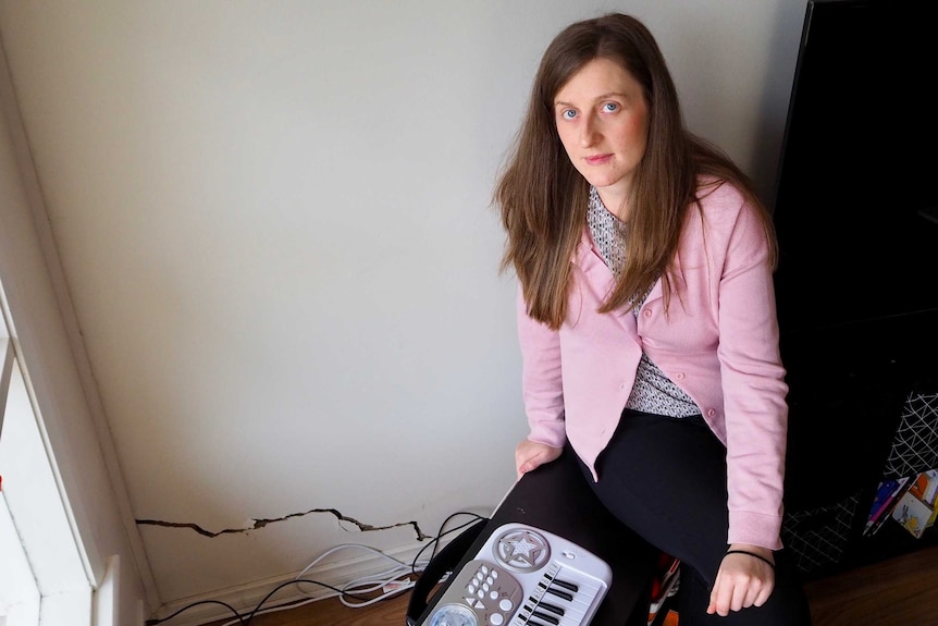 Amy Zuccon sits beside a large crack in the wall of her unit.