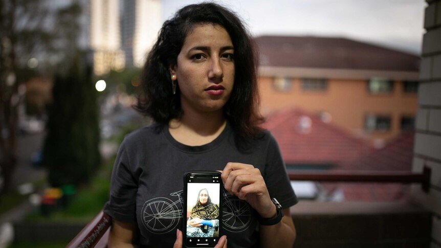 A woman standing on a balcony holding up a mobile phone.