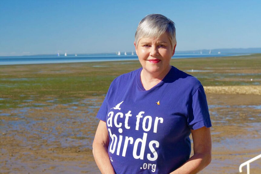 Judith Hoyle stands outside near wetlands wearing an 'act for birds.org t-shirt.
