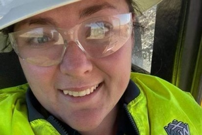 A woman wearing high-vis clothing, safety glasses and a hard hat gives a thumb's up in a selfie.