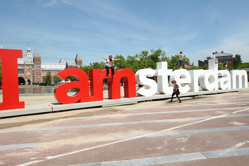 A person poses for a photo atop giant letters that say 'I Amsterdam'