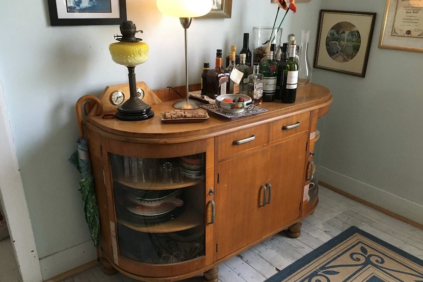 A wooden and glass sideboard unit holds lamps, alcohol and crockery in an older home.