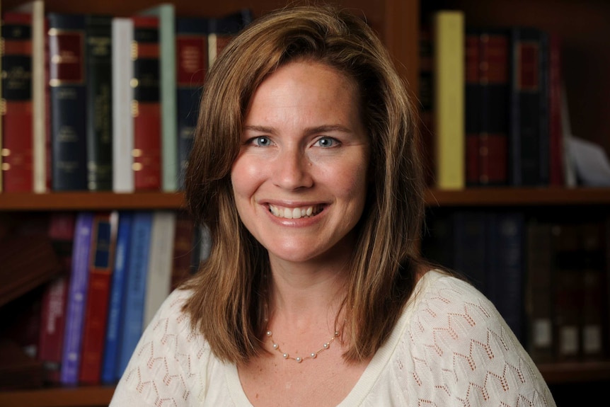 A portrait of Amy Coney Barrett smiling in front of a book case