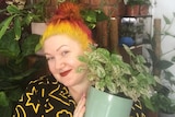 A woman proudly holds an indoor plant, in a story about how often to change plant potting mix.