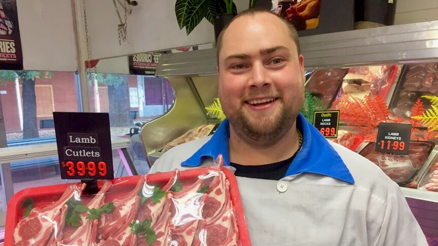 A butcher holding a tray of lamb cutlets