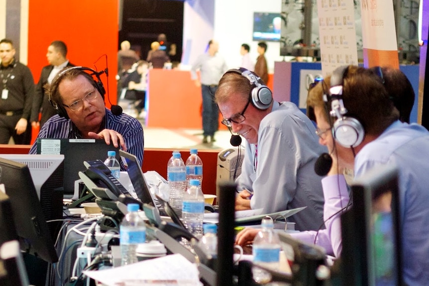 Colvin and Faulkner with head sets on sitting at desk in front of laptops.