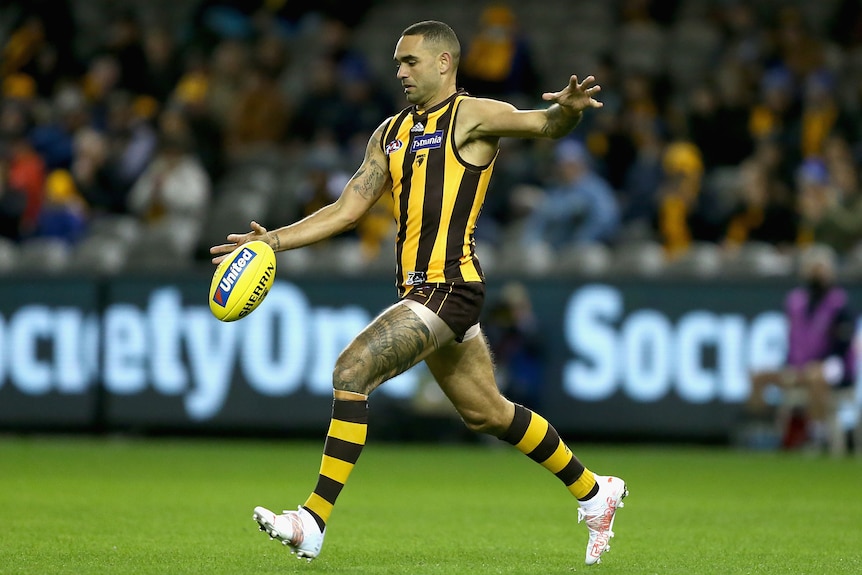 A Hawthorn AFL player prepars to kick the ball with his right foot against Port Adelaide. 