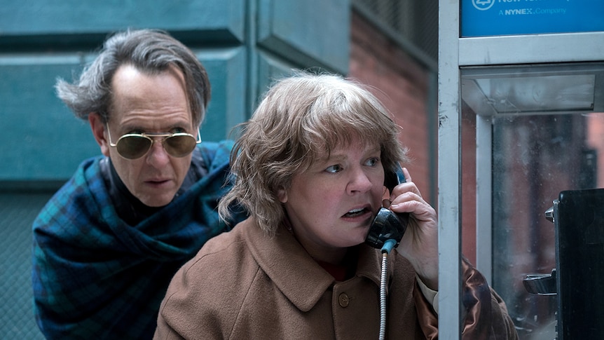 Colour still of Richard E. Grant and Melissa McCarthy taking a call at a phonebooth in 2018 film Can You Ever Forgive Me?