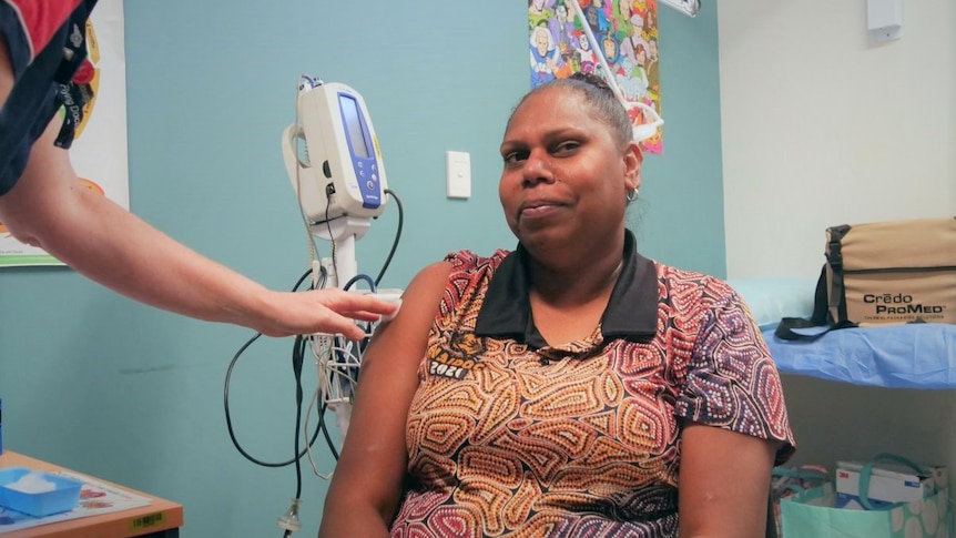 An Aboriginal woman looks at the camera while a nurse touches her arm after getting a vaccine