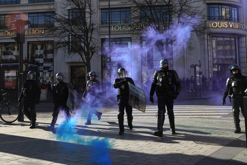 French riot police stand amidst tear gas during a protest on the Champs-Elysees avenue.
