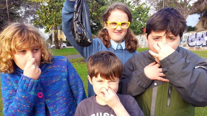 Four children holding their noses while holding a bag of dog poo.