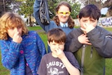 Four children holding their noses while holding a bag of dog poo.