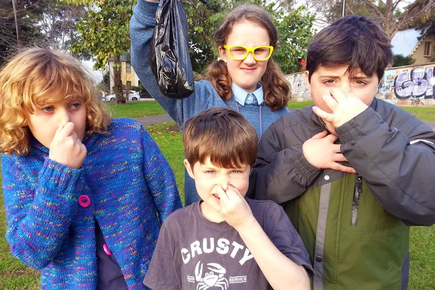 Four children holding their noses while holding a bag of dog poo.