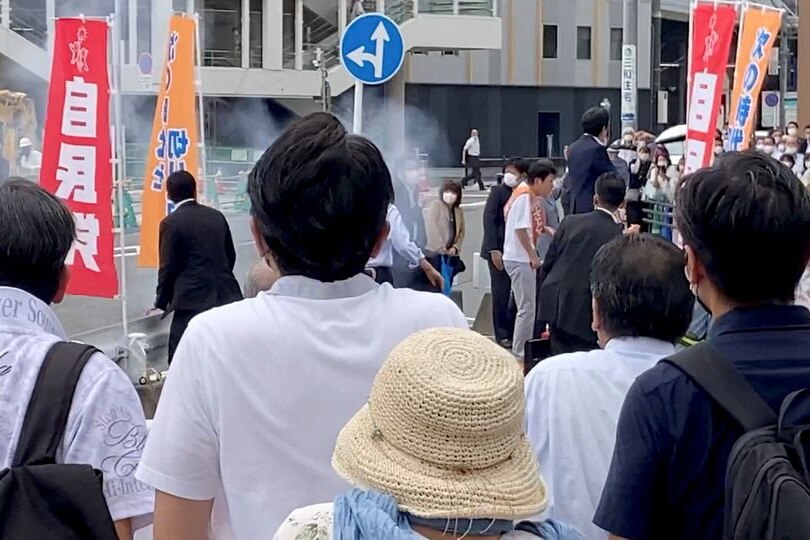 People stand on a crowded japan street as a cloud of smoke billows out above a politician 