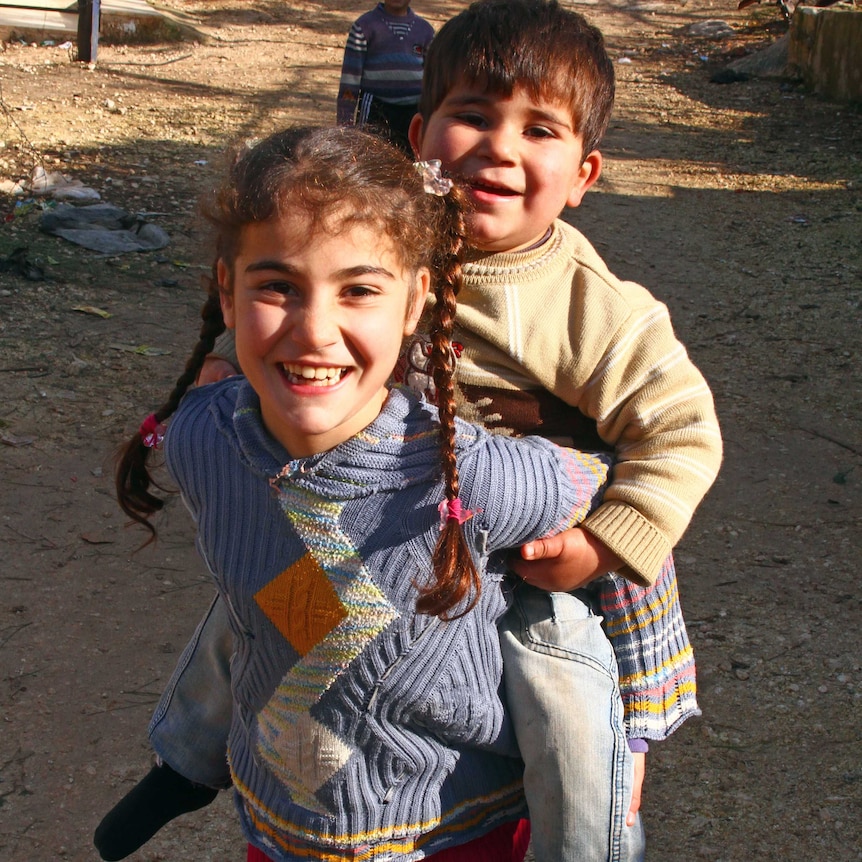 A girl laughs holding a small boy on her back.