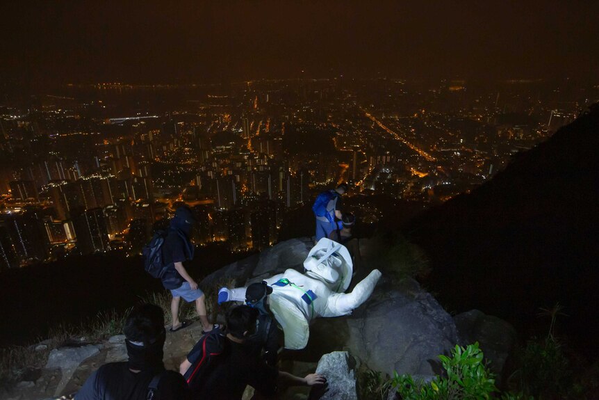 Protestes lay a white statue on a rock atop the peak, looking out over the glittery skyline