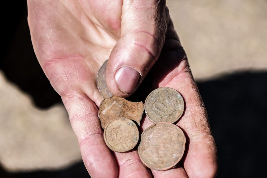 A close-up of old coins dug up from the ground, in a man's hand.