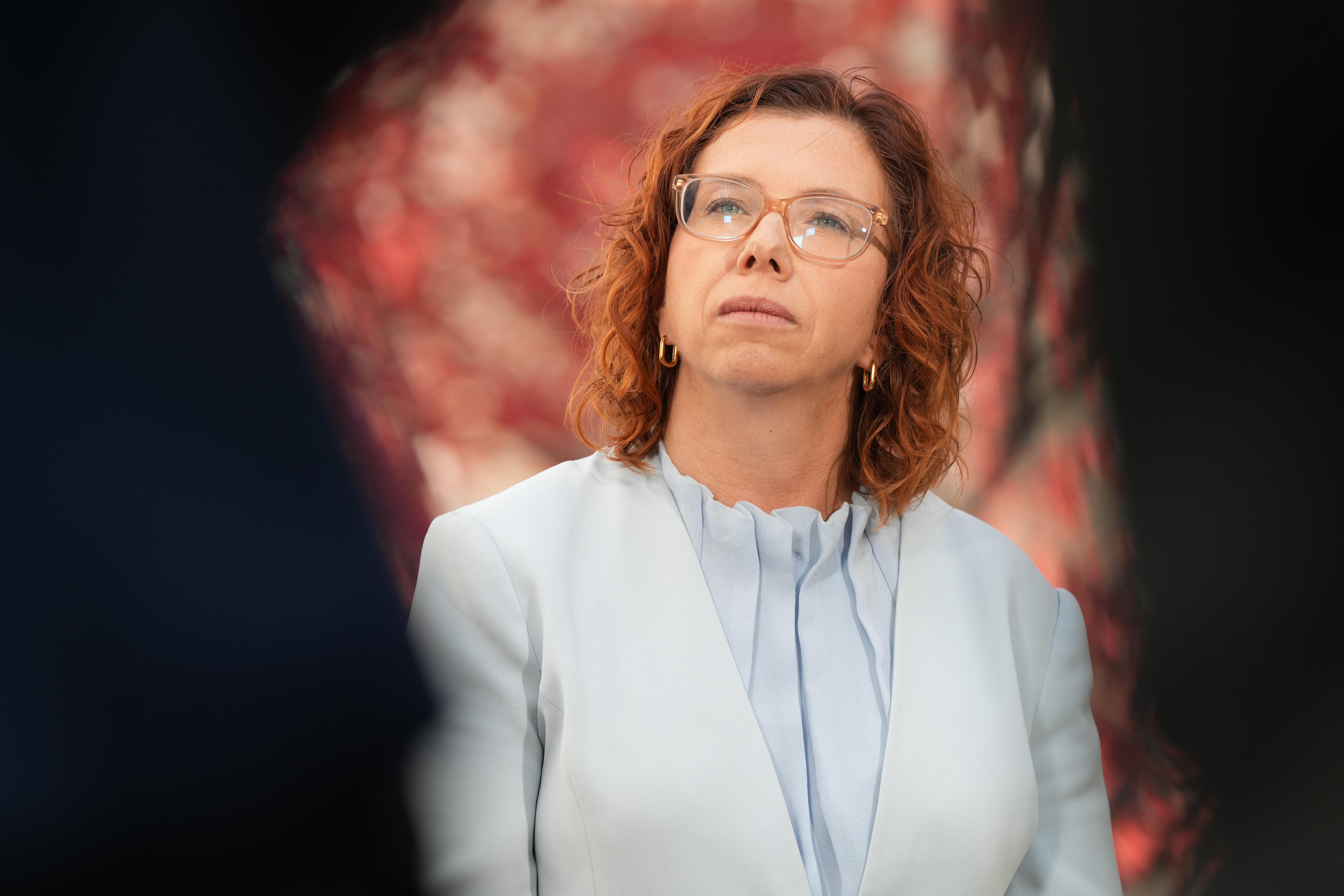 Amanda Rishworth wears a light blue blouse standing outside with red leaves in the background.