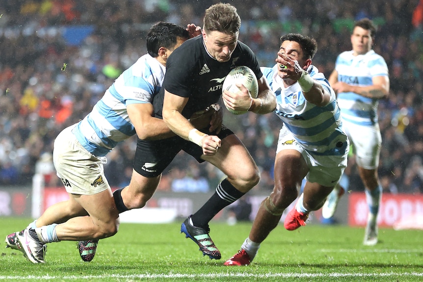 An All Blacks player scores a try as he is tackled by two Pumas players.
