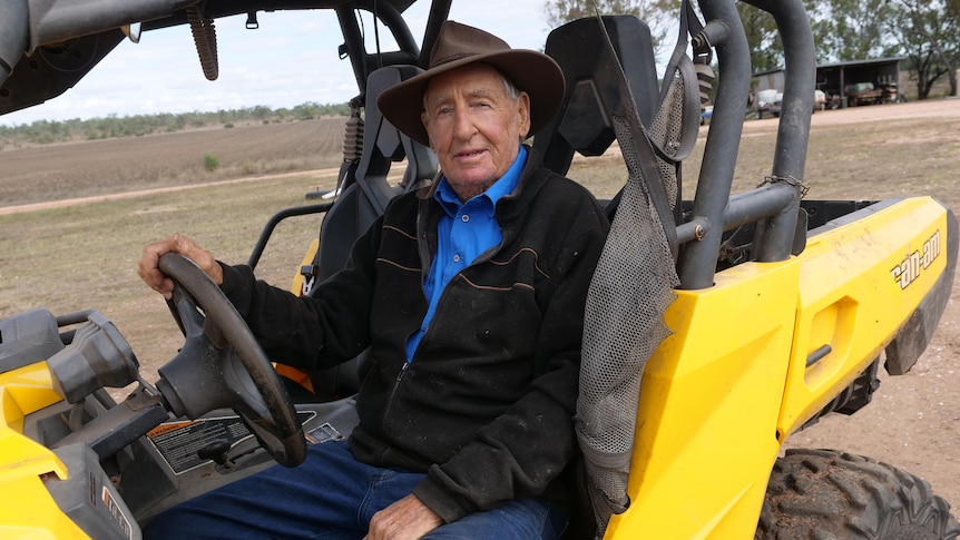 An older man sits in a yellow buggy with his hand on the steering wheel
