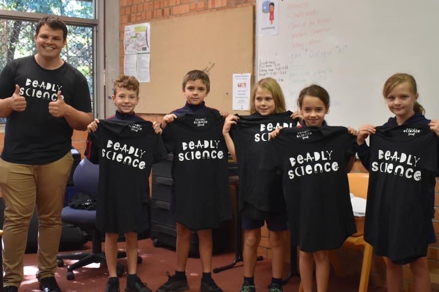 A man in a "Deadly Science" T-shirt stands alongside school students wearing T-shirts with the same design.