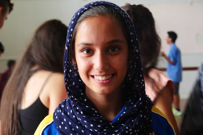 A smiling young woman in  a spotted headscarf looks straight at the camera