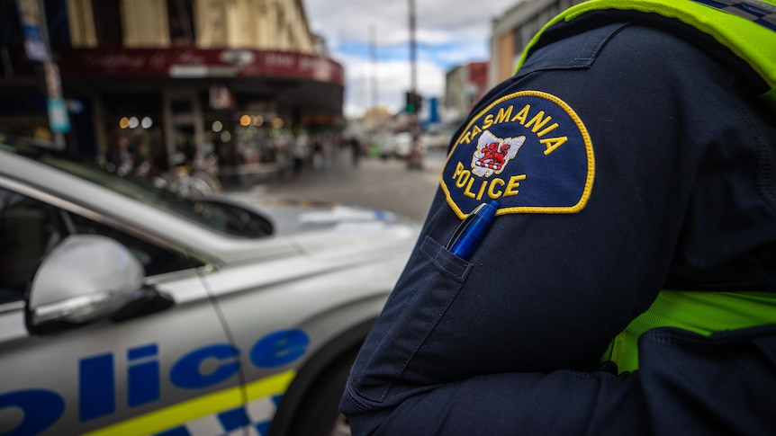 A Tasmania Police officer stands in front of a patrol car in Hobart's CBD.