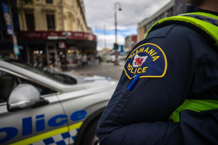 A Tasmania Police officer stands in front of a patrol car in Hobart's CBD.