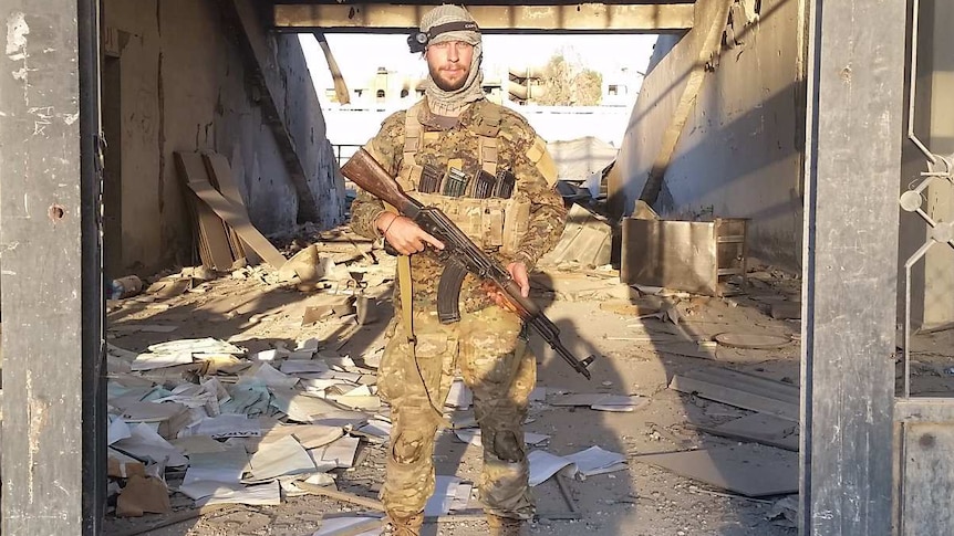 Jamie Williams stands in the doorway of a stadium and holds a gun.