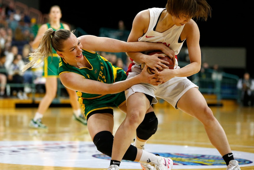 Tess Madgen is falling down, trying to prise the basketball out of her opponent's hands.