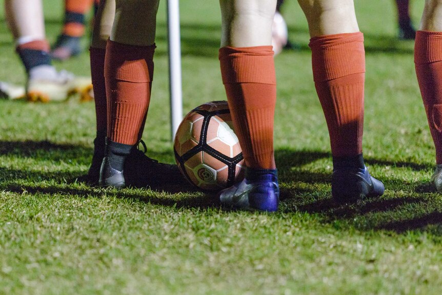 A tight shot of the legs of two Northern Redbacks Women's Soccer Club under 16s players with red socks on and a ball.
