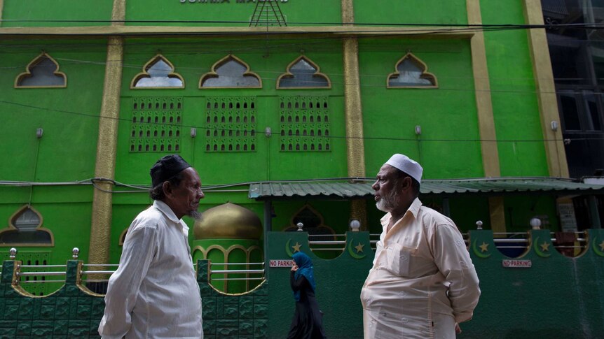 Two Sri Lankan Muslims stand outside a bright green mosque in Colombo.