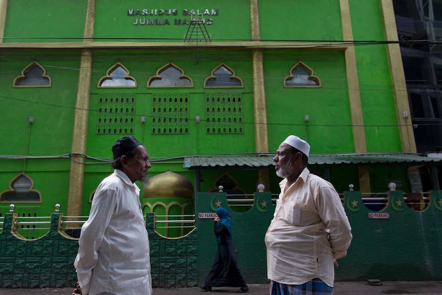 Two Sri Lankan Muslims stand outside a bright green mosque in Colombo.