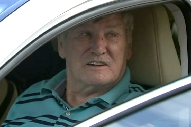 A man in a green striped t-shirt sits in a car.