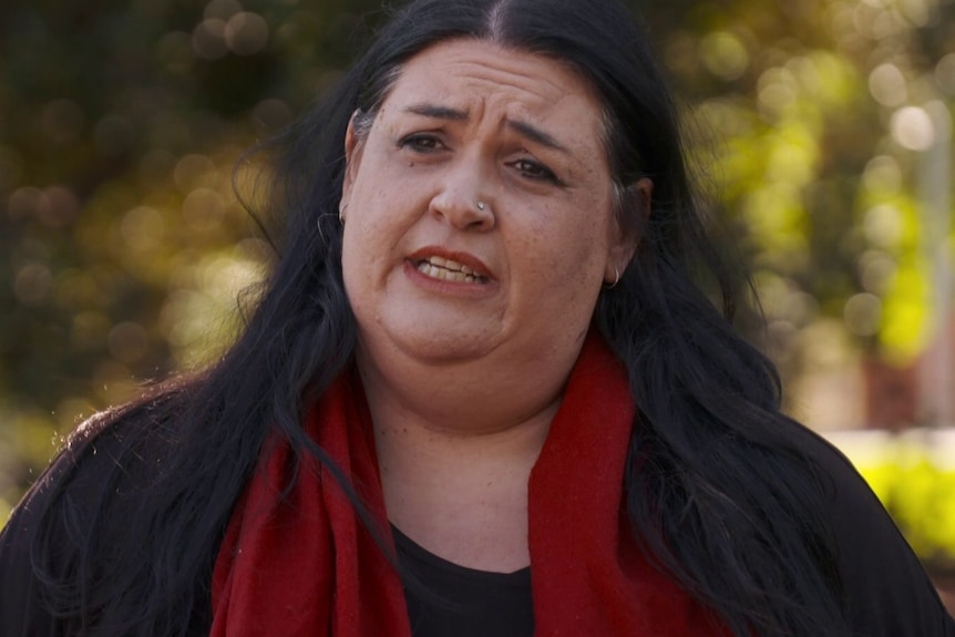 Woman wearing black cardigan and red scarf, talking to a journalist.