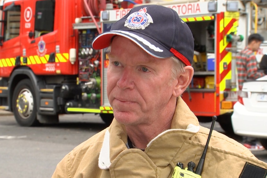 Paul wearing a firefighter uniform standing in front of a firetruck. 