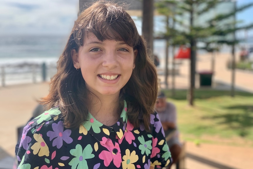 A young girl with dark hair, smiling at the beach.