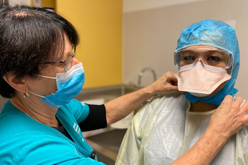 A nurse helps another nurse with her PPE.