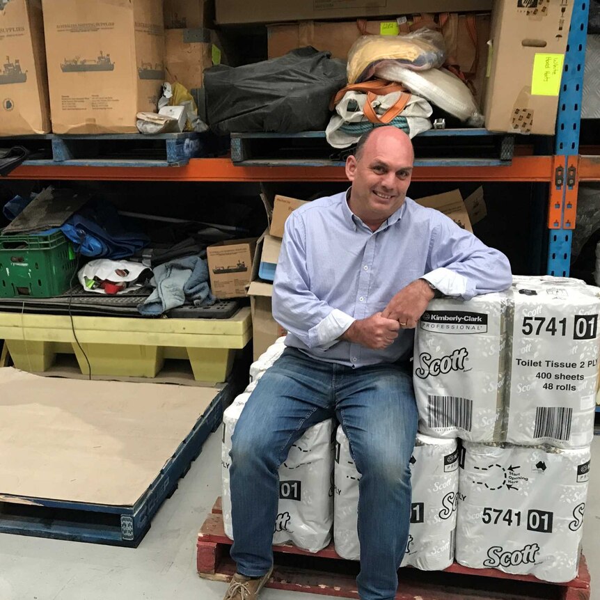 Richard Fader sitting on a pile of toilet paper in the Tasmanian Shipping Supplies warehouse