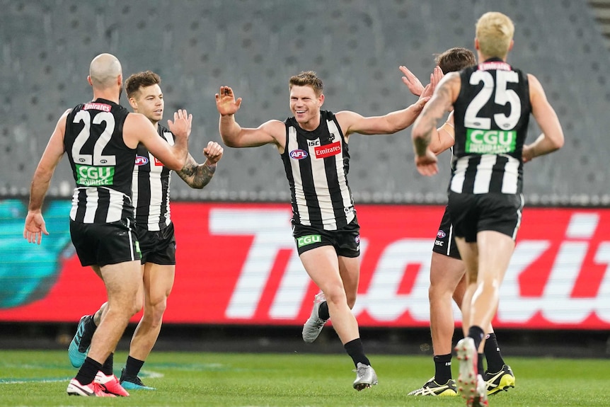A grinning AFL player holds his hands up to high five teammates after kicking a goal.