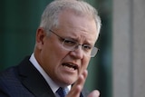 Scott Morrison holds his arm out while making a point. He's speaking in his courtyard in a blue tie