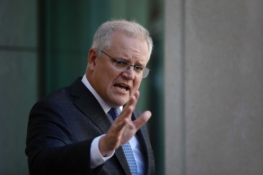 Scott Morrison holds his arm out while making a point. He's speaking in his courtyard in a blue tie