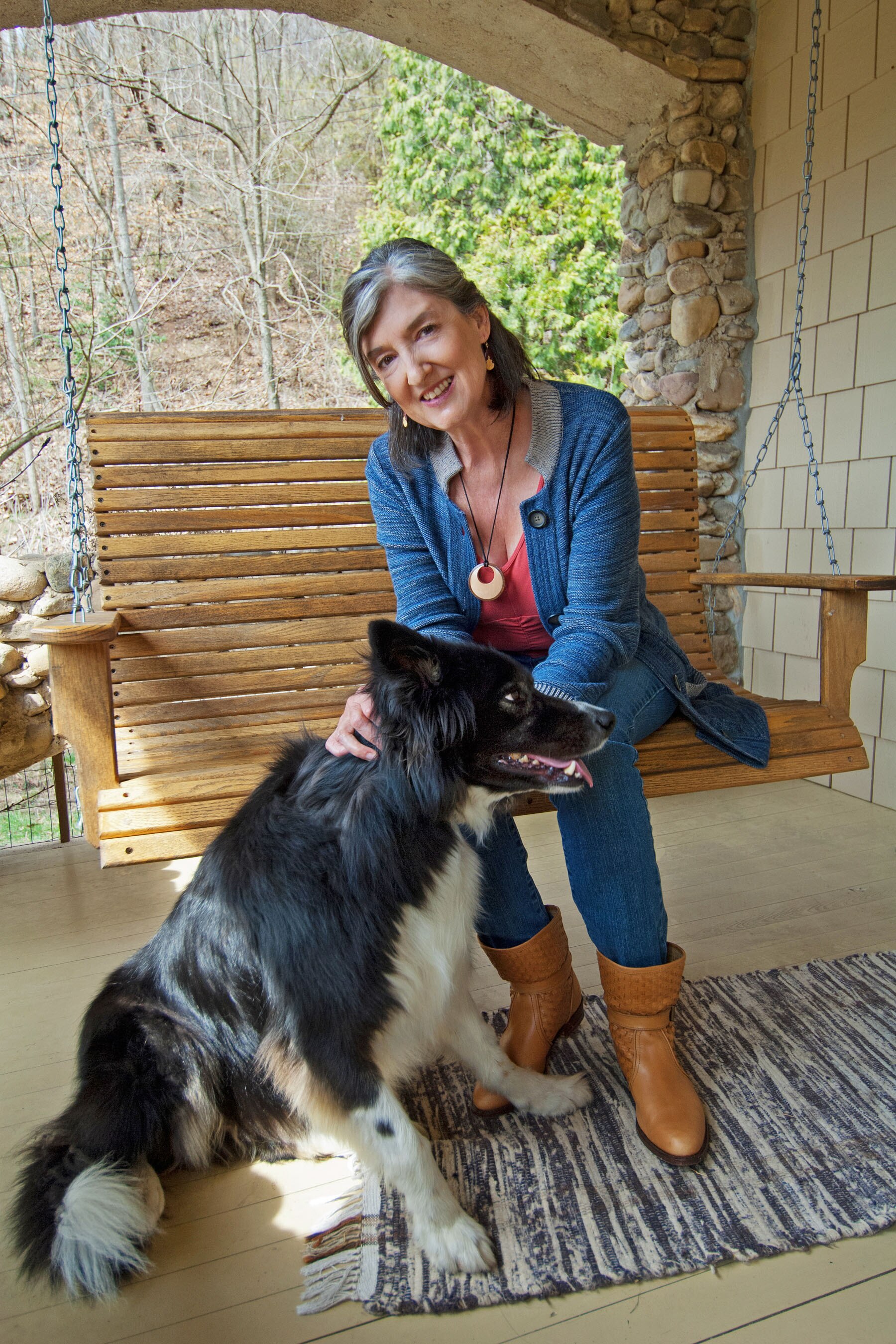 A grey-haired woman wearing a blue cardigan sits and pats a black and white dog