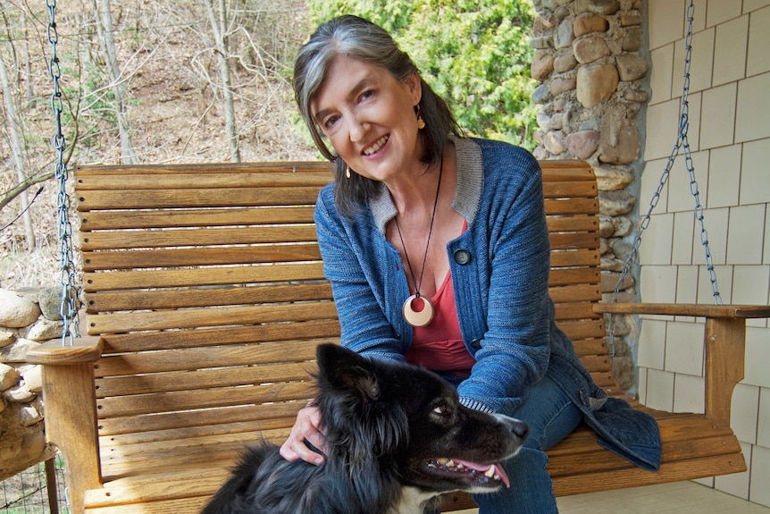 A grey-haired woman wearing a blue cardigan sits and pats a black and white dog