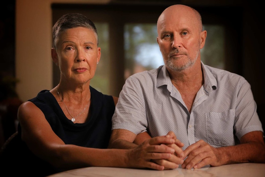 Karen and John Bird sit at a table holding hands.