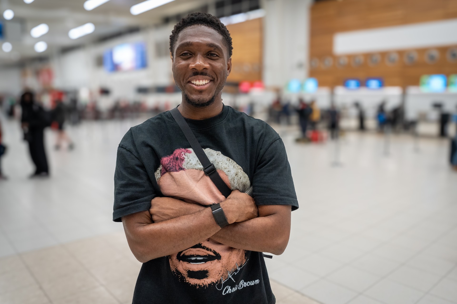 A man with a sling bag and his arms crossed smiles at the departure hall of Adelaide Airport