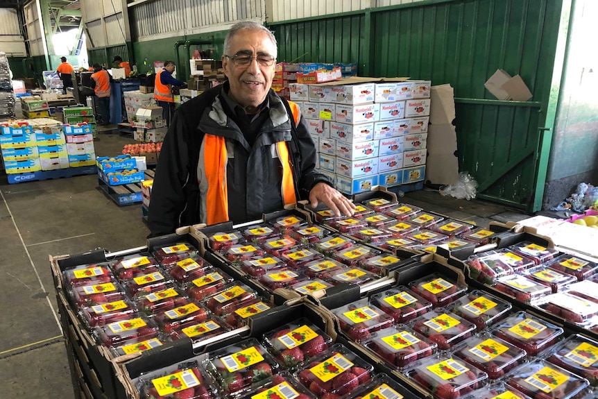 A man with grey hair standing behind a tray of strawberries in a warehouse.