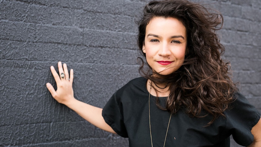 Sexologist and yoga teacher Vanessa Muradian leans against a dark brick wall.