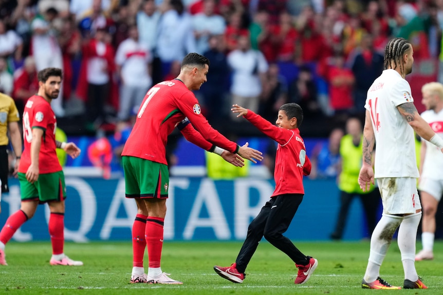 Cristiano Ronaldo reaches out to hug a young boy who has run on the field during a game